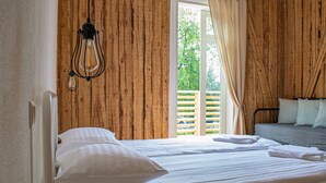 A bedroom with a wooden wall, a bed with white bedding, a hanging light fixture, and a view of a wooden deck outside. - TAEAVS  (Võru)
