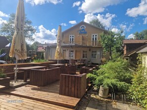 Eine Holzterrasse mit Sitzgelegenheiten, ein Gebäude mit dem Schild "Tavern" und ein klarer, blauer Himmel.