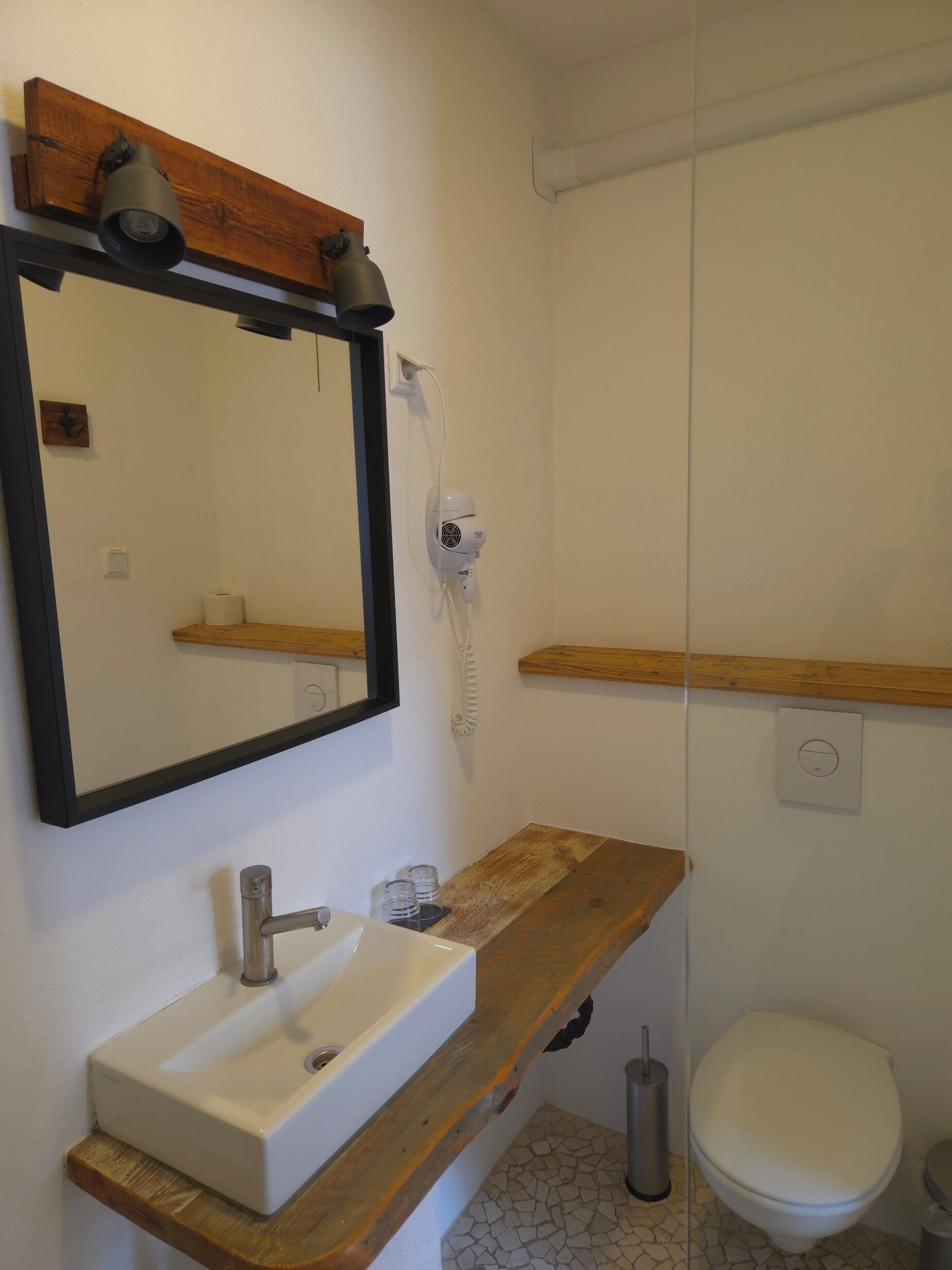 A bathroom with a wooden vanity, a white sink, a mirror, a toilet, and a shower area.