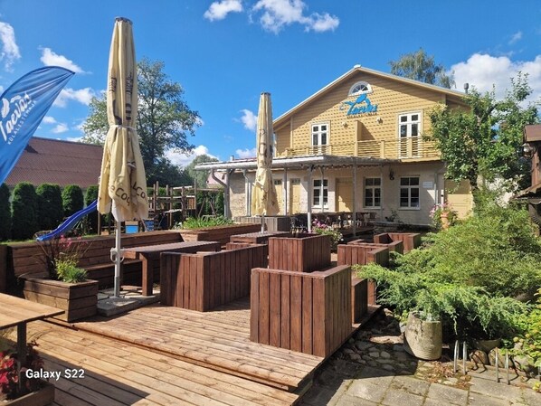 Eine Holzterrasse mit Sitzgelegenheiten, ein Gebäude mit Schild und eine blaue Flagge.
