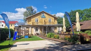 A yellow building with a sign reading "Hotel". There is a blue slide in the foreground, and a garden with various plants and flowers. - TAEAVS  (Võru)