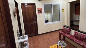 A living room with a wooden floor, a sofa, a small table, a fan, and a window. - Morocco Hotel El Nido  (El Nido)