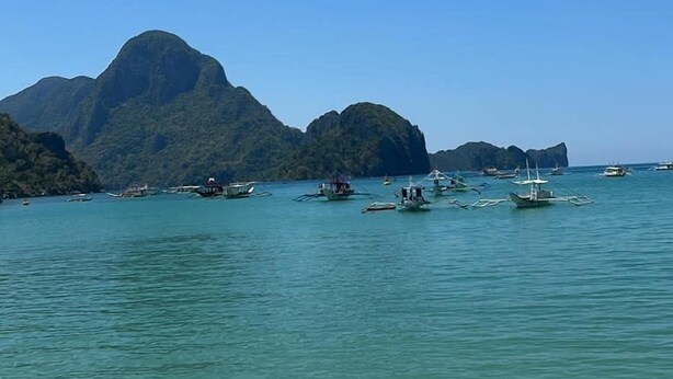 A beach with clear turquoise water, boats, and mountains in the background. - Morocco Hotel El Nido  (El Nido)