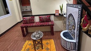 A room with a wooden floor, a red and beige patterned sofa, a small table with metal trays, a decorative wall with a geometric pattern, and a staircase with black railings. - Morocco Hotel El Nido  (El Nido)