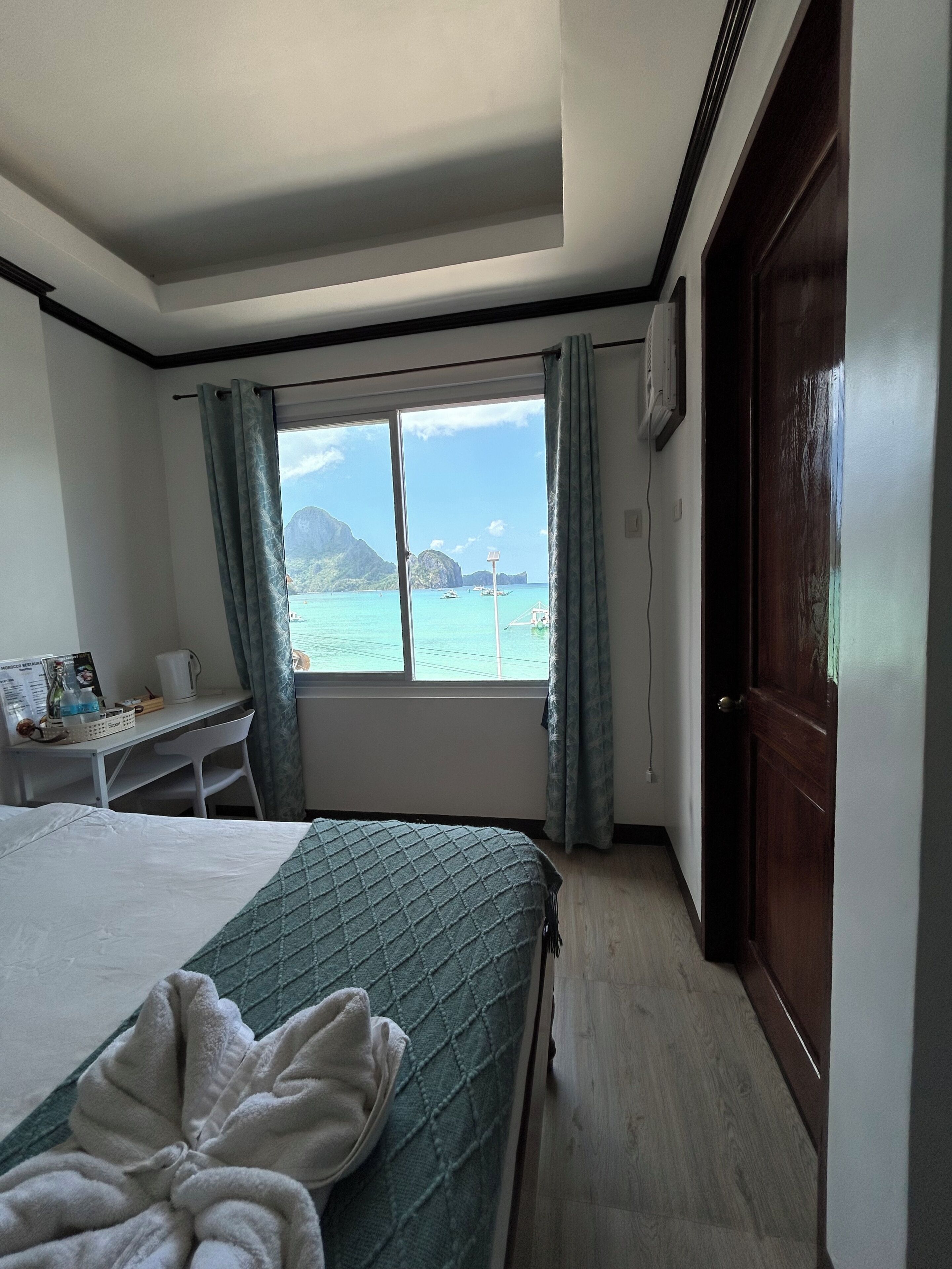 Habitación de hotel con cama, escritorio, vista al mar y puerta de madera.