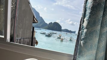 Una habitación con ventana que da a una masa de agua, una silla blanca, una taza de colores y una pequeña mesa con cuchara y soporte para servilletas.