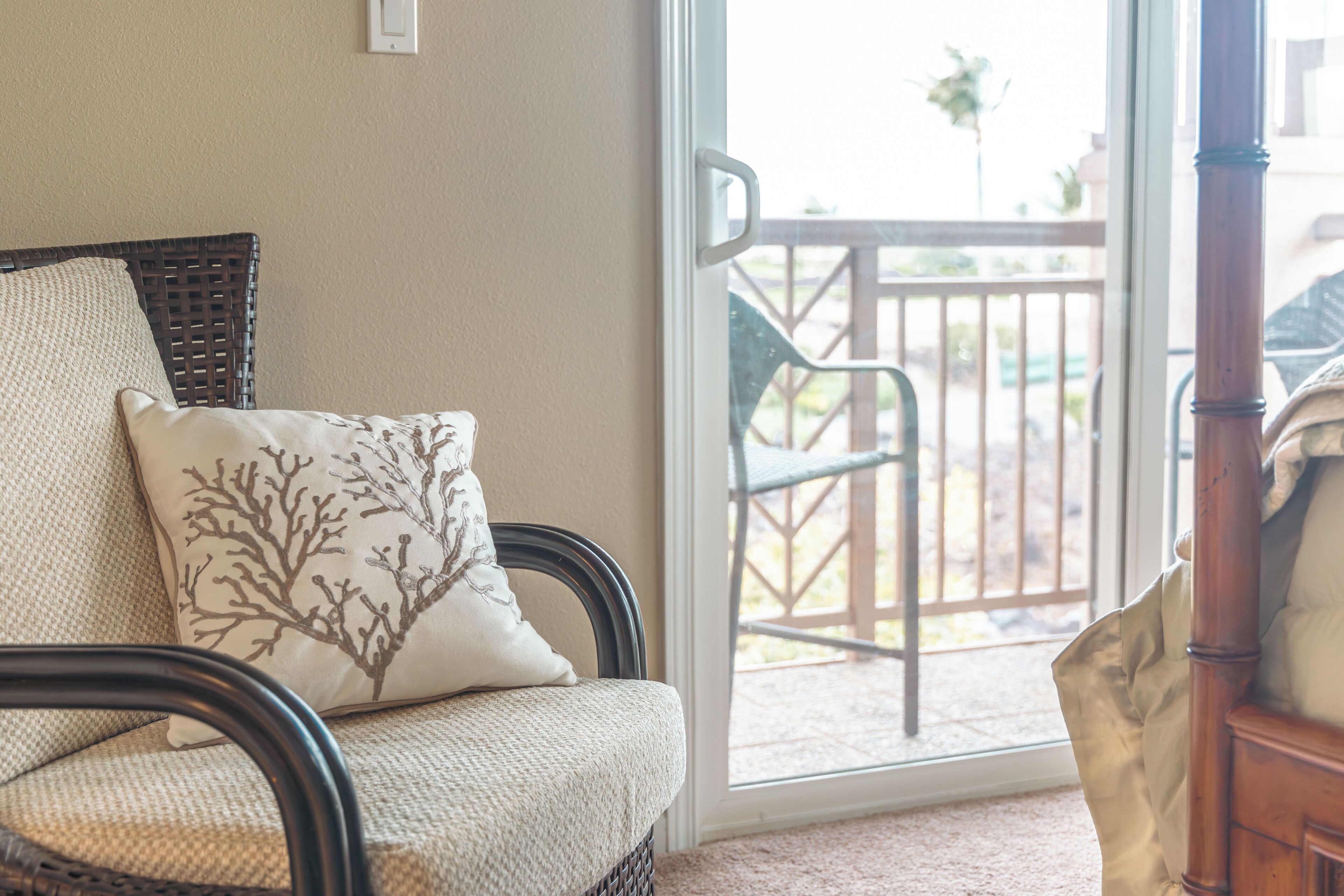 A wicker chair with a cushion, a wooden chair, and a view of an outdoor patio with a railing and chairs.