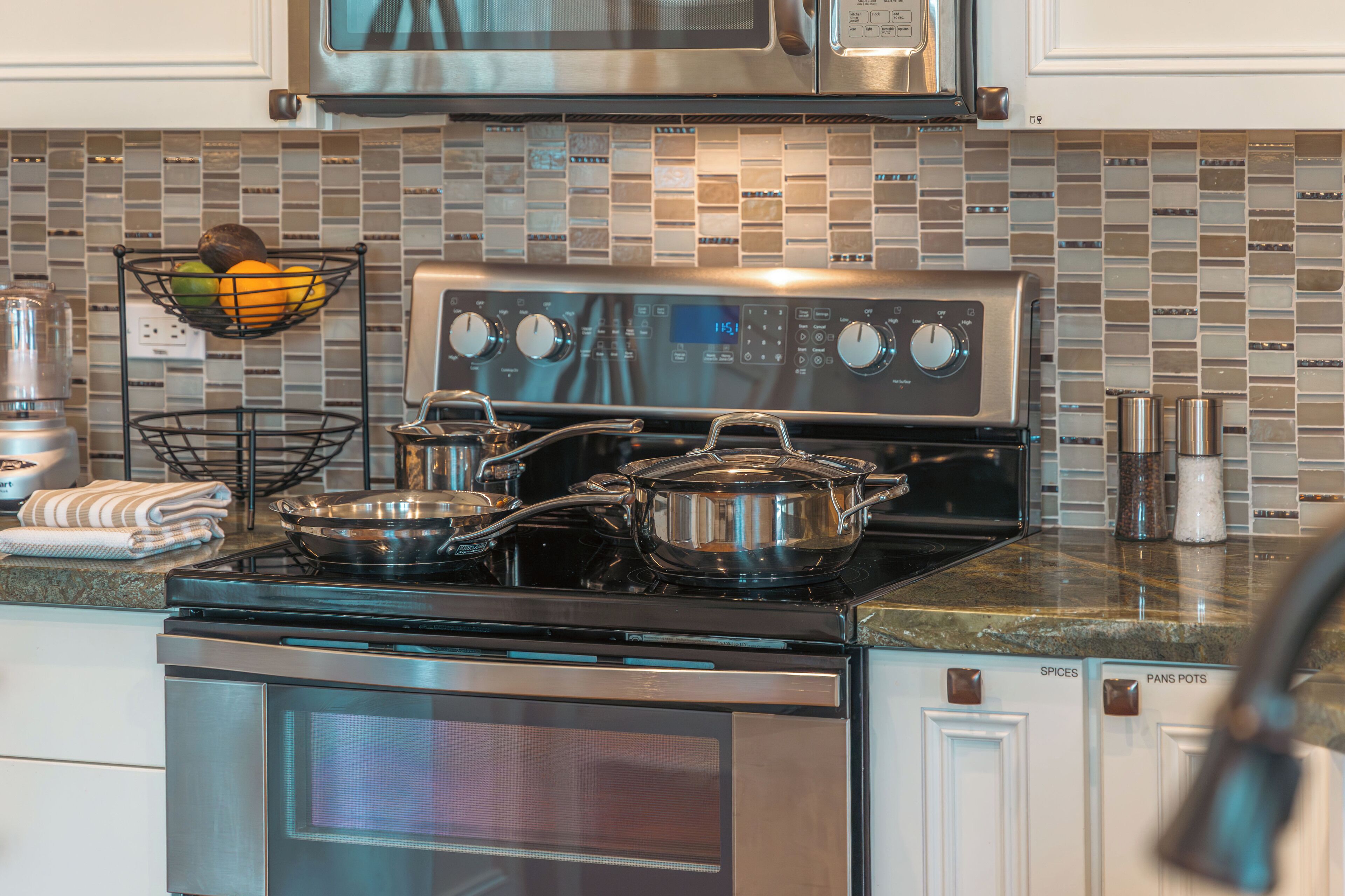 A kitchen with a stainless steel stove, oven, and microwave. There are pots on the stove, a fruit basket, and a spice rack.