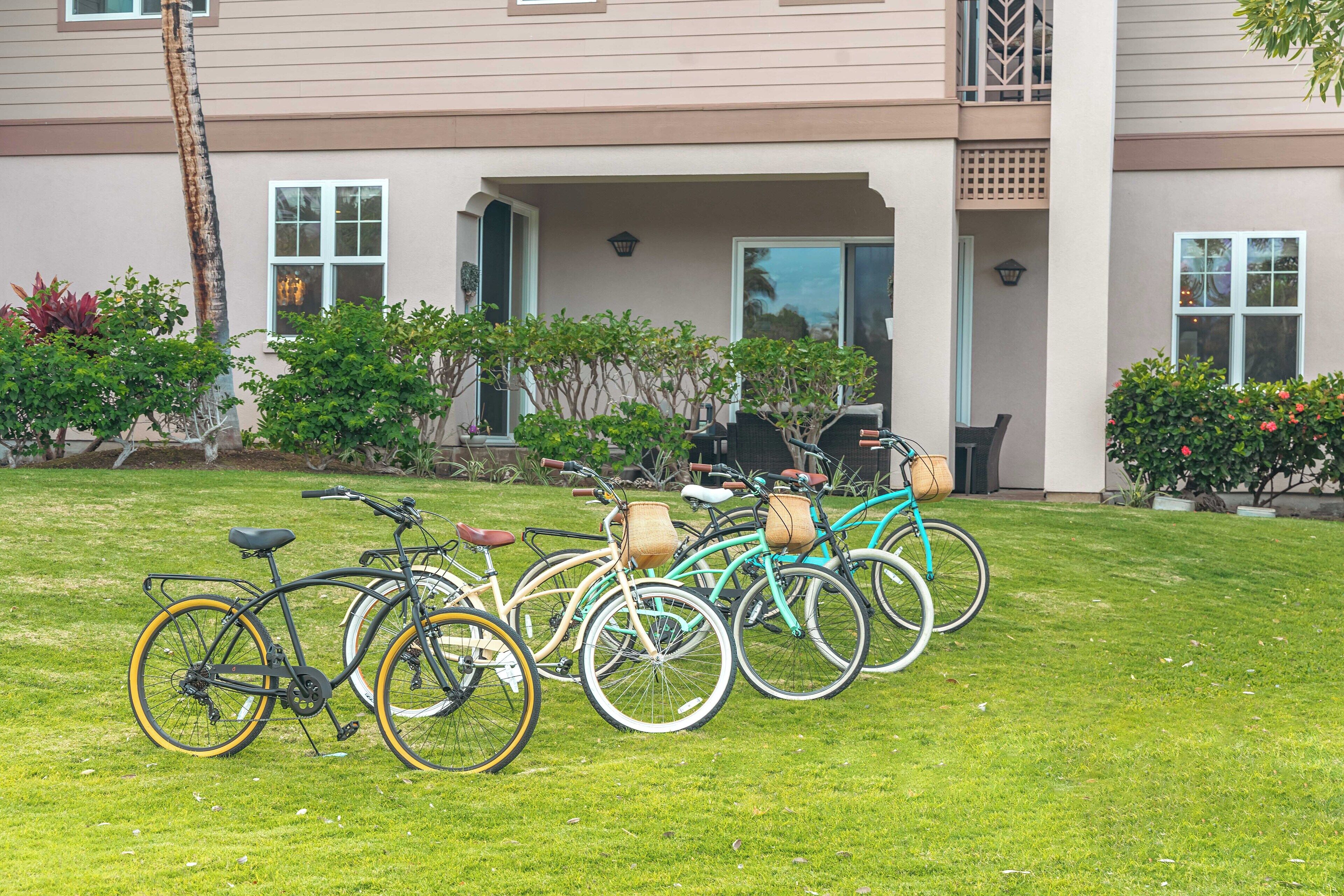 A row of bicycles parked on a lawn in front of a building with a covered patio area.
