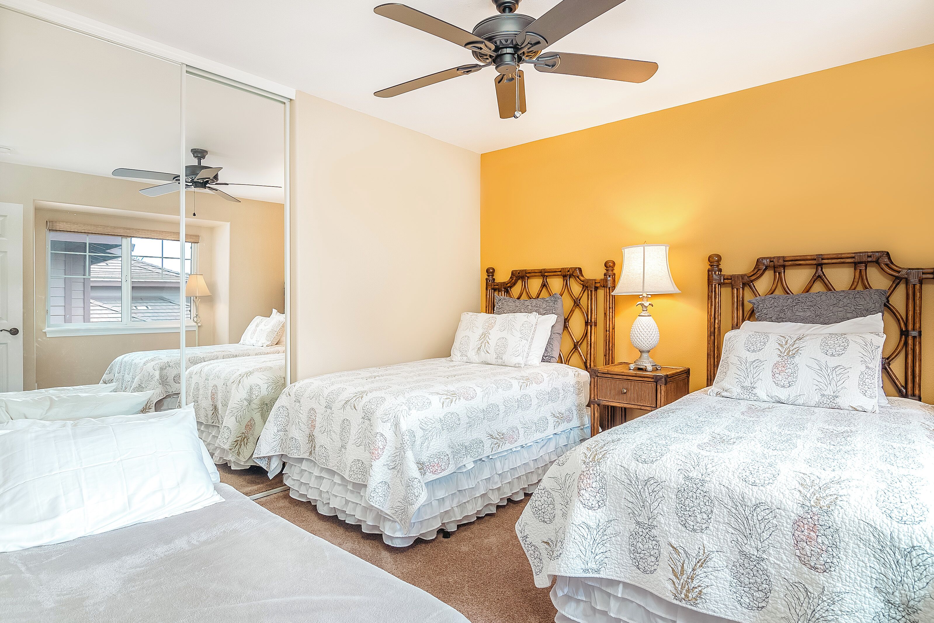 A hotel room with three single beds, a ceiling fan, a bedside lamp, and a large mirror.
