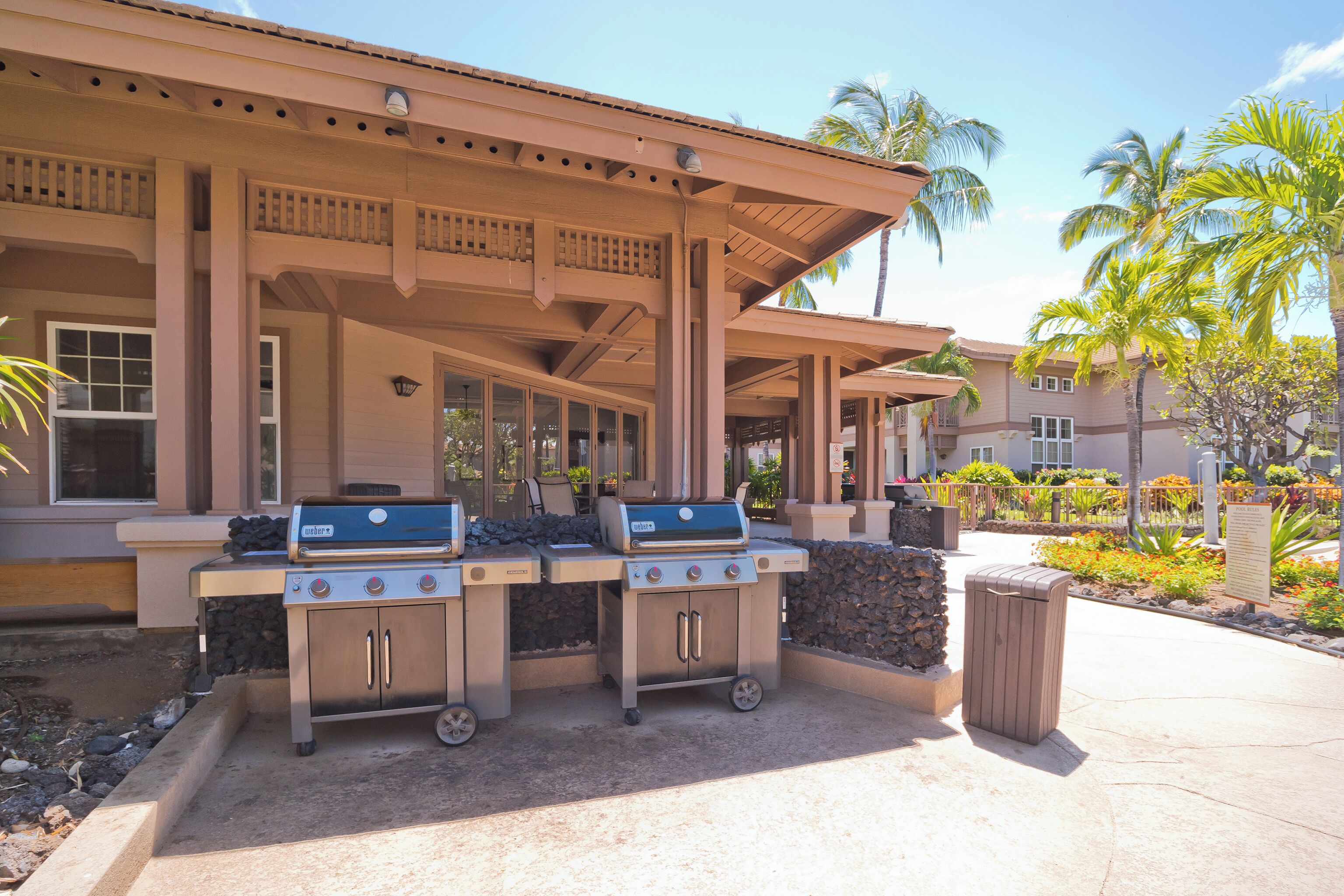 An outdoor patio with two barbecue grills, a trash can, and a stone planter.