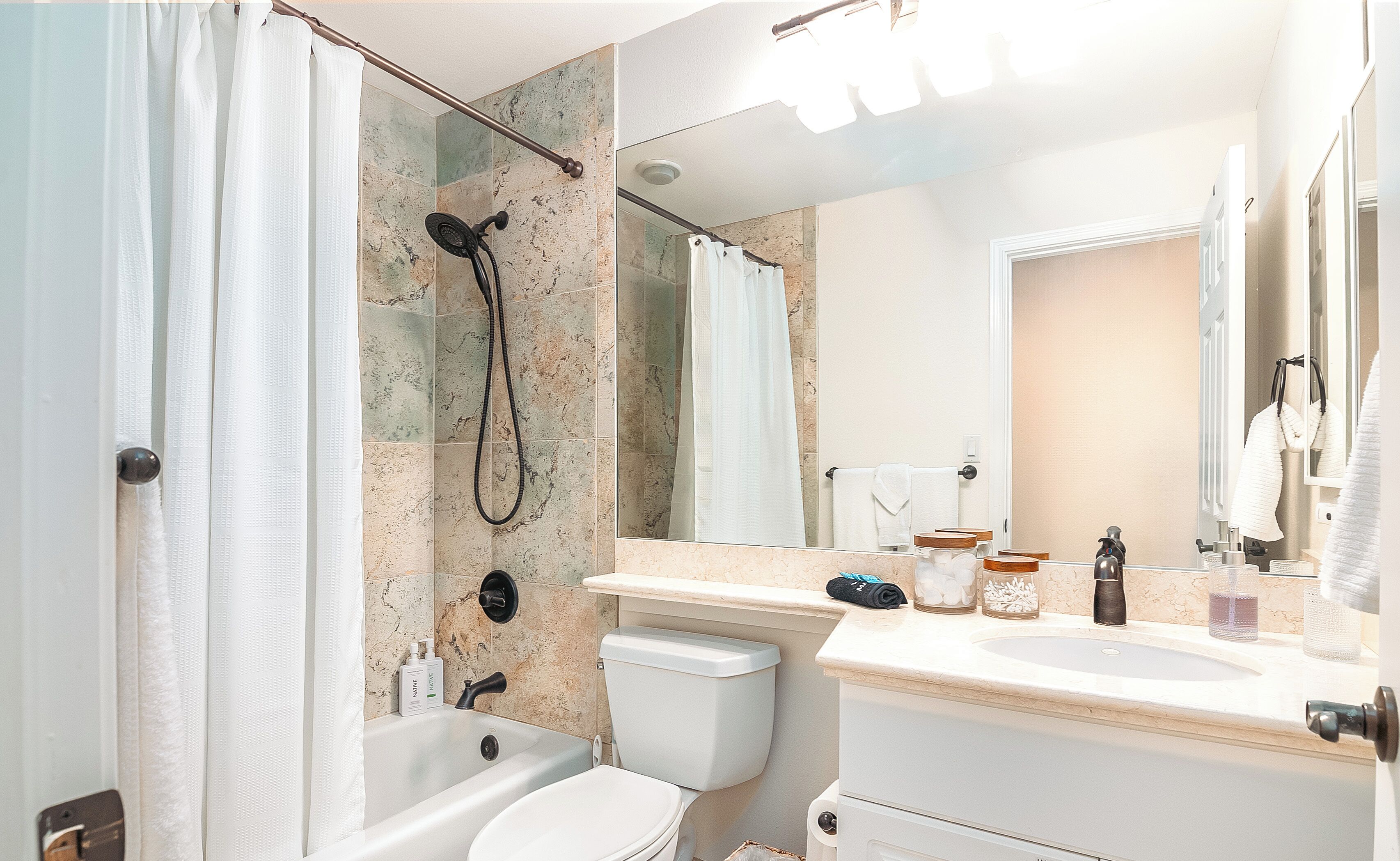 A bathroom with a shower, toilet, sink, and a large mirror.