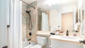 A bathroom with a shower, toilet, sink, and a large mirror.
