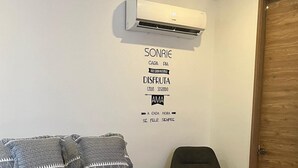 Un dormitorio con cama, una silla, un equipo de aire acondicionado y una puerta de madera.