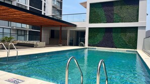 Un hotel moderno con piscina, techo de madera y pared verde con diseño de árbol.
