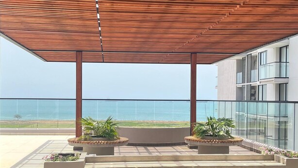 Una terraza exterior con techo de madera, plantas en macetas y vista al mar.