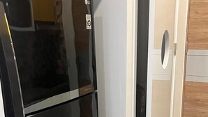 Una cocina con un refrigerador negro, un cesto de basura y una puerta de madera.