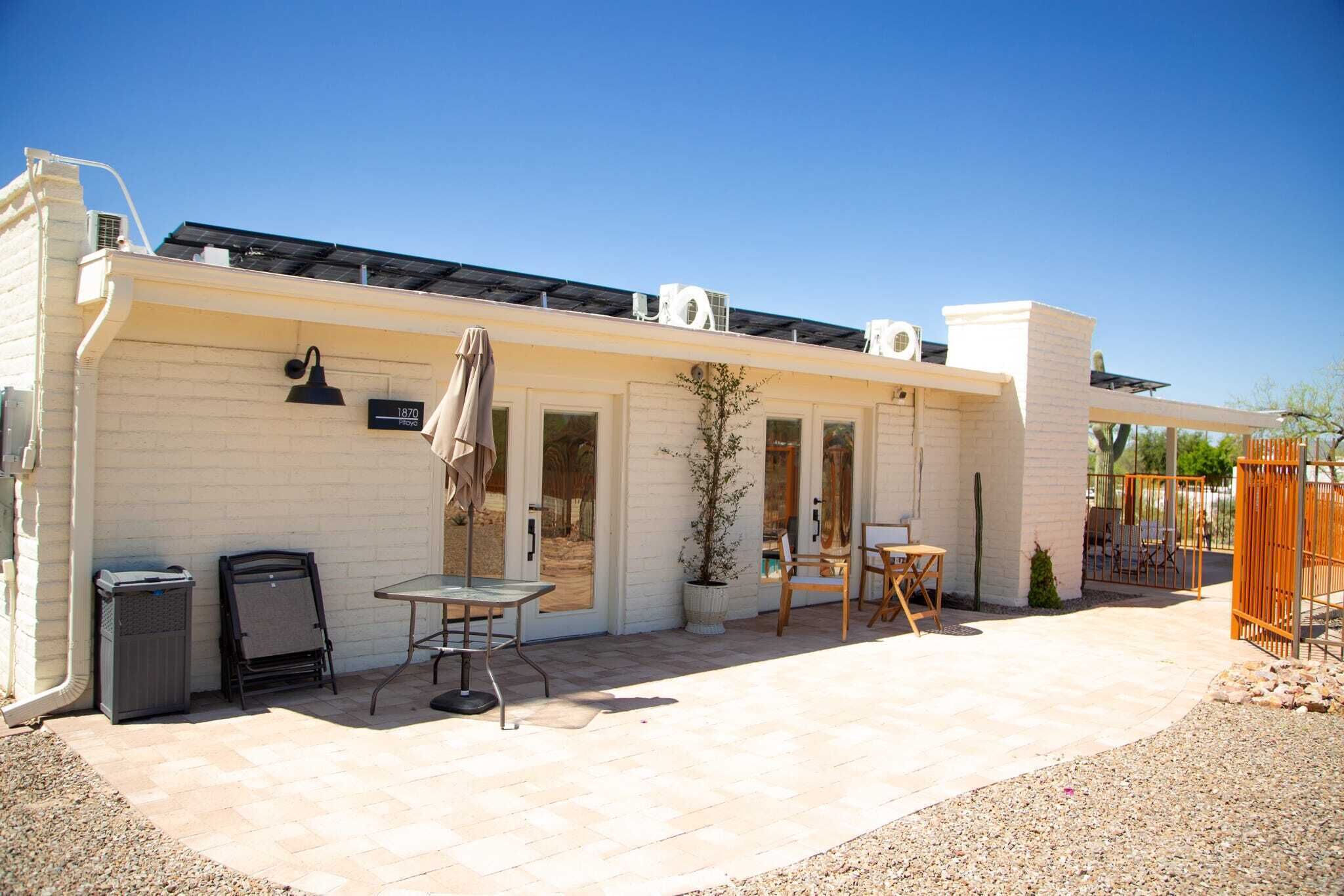 A white building with a patio area, outdoor seating, and a small garden.