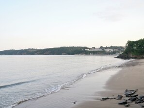 A beach with calm waters, a sandy shore, and buildings in the background. - The Garden Lodge Flat - UK49415 (LLanteg, near Narbeth)