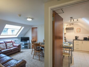 A cozy living room with a leather sofa, a dining table with chairs, a TV, and a skylight. - The Garden Lodge Flat - UK49415 (LLanteg, near Narbeth)