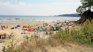 A beach with tents and umbrellas, sandy beach, and a cliff with trees.