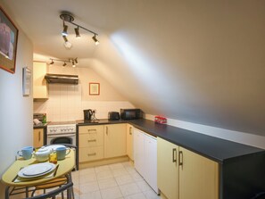 Une cuisine compacte équipée d’une cuisinière à gaz, d’un four à micro-ondes, d’un grille-pain et d’une petite table à manger pour deux personnes.