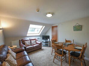 A cozy living room with a brown leather sofa, a dining table with chairs, a television, and a skylight.