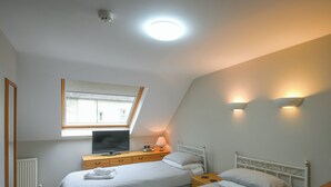 A bedroom with two beds, a TV, a window, and a ceiling light.
