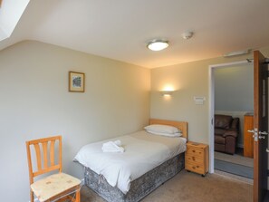 Un dormitorio con una cama individual, una silla de madera, una mesita de noche, un espejo y una puerta que da a otra habitación.