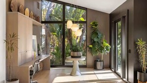 A modern interior with a large window, a central table, and various potted plants. - Hollywood Hills Villa by Universal-Pool-Dogs OK (Los Angeles)