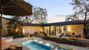 A modern outdoor pool area with a lounge chair, a dining table, and a covered patio. - Hollywood Hills Villa by Universal-Pool-Dogs OK (Los Angeles)