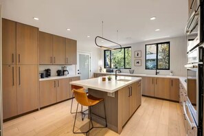 Een moderne keuken met houten kasten, een centraal eiland met zitplaatsen en een groot raam voor natuurlijk licht.