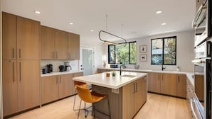 A modern kitchen with wooden cabinets, a central island with seating, and a large window providing natural light. - Hollywood Hills Villa by Universal-Pool-Dogs OK (Los Angeles)