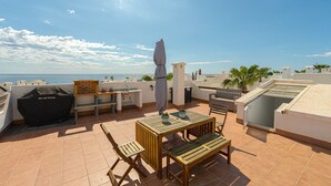A rooftop terrace with a wooden table and chairs, a grill, and a view of the sea. - Apartamento La Isla (Mar de Pulpi) (San Juan de los terreros)