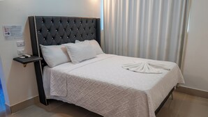 Una cama bien hecha con un edredón blanco acolchado y una toalla doblada al pie.