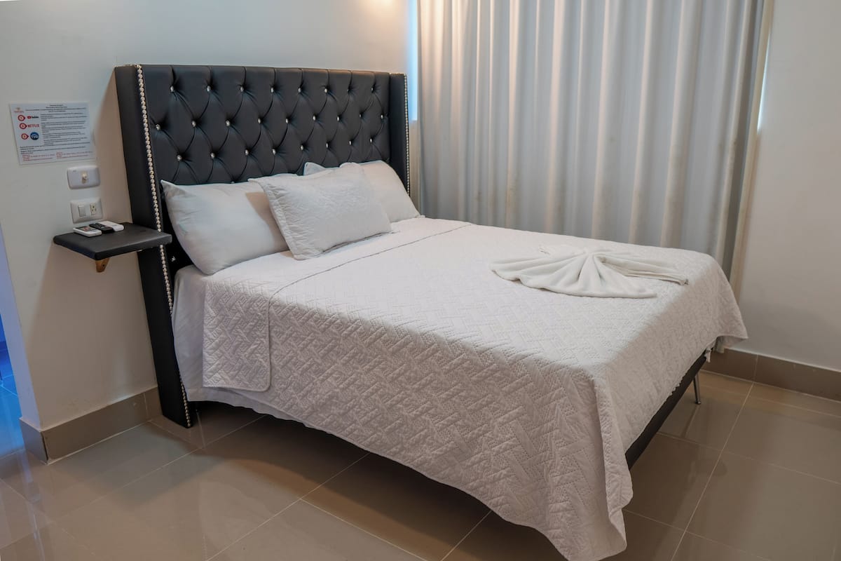 A neatly made bed with a quilted white bedspread and a folded towel at the foot.