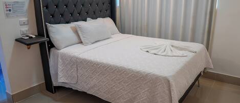 A neatly made bed with a quilted white bedspread and a folded towel at the foot.