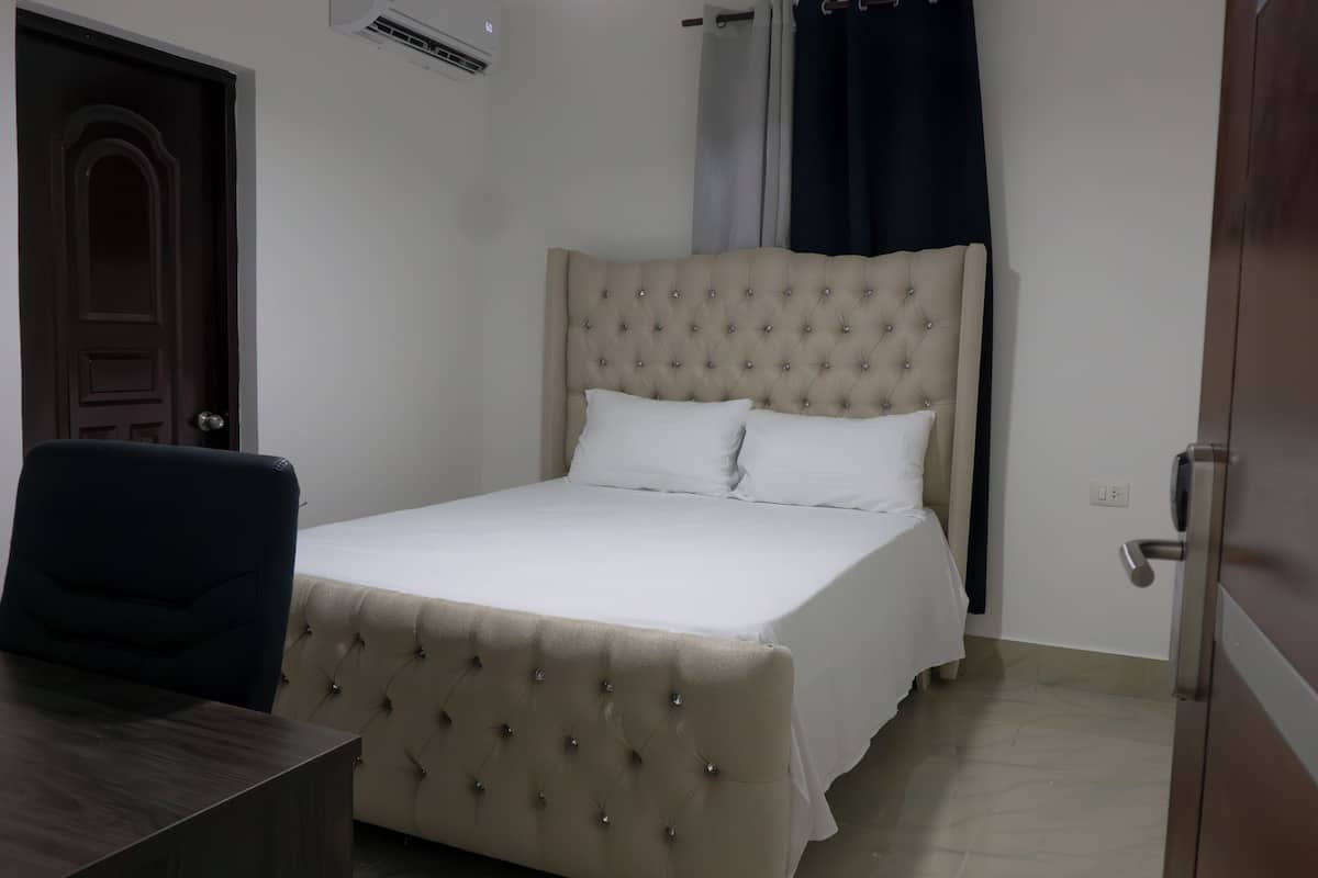 A bedroom with a bed, a chair, a desk, and a door.