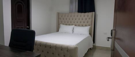 A bedroom with a bed, a chair, a desk, and a door.