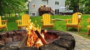 A backyard with a fire pit, yellow Adirondack chairs, and a house in the background. - 4bdr 2 bath house. Unwind in the hot tub, chat around the fire pit and disc golf (Traverse City)
