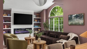 A living room with a large flat-screen TV, a brown sofa, a green armchair, and a wooden coffee table. - 4bdr 2 bath house. Unwind in the hot tub, chat around the fire pit and disc golf (Traverse City)