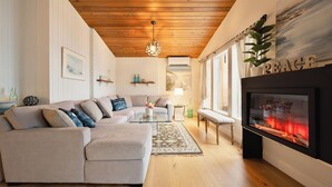 Ein Wohnzimmer mit Ecksofa, Glastisch, Kamin und Holzboden.