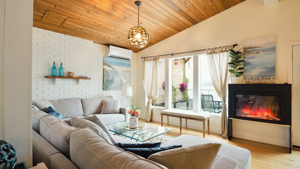 Ein Wohnzimmer mit einer Couch, einem Glastisch, einem Kamin und Blick ins Freie.