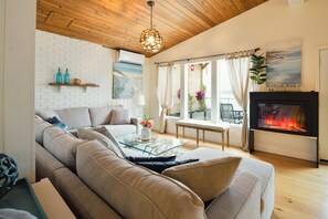 Ein Wohnzimmer mit einer Couch, einem Glastisch, einem Kamin und Blick ins Freie.