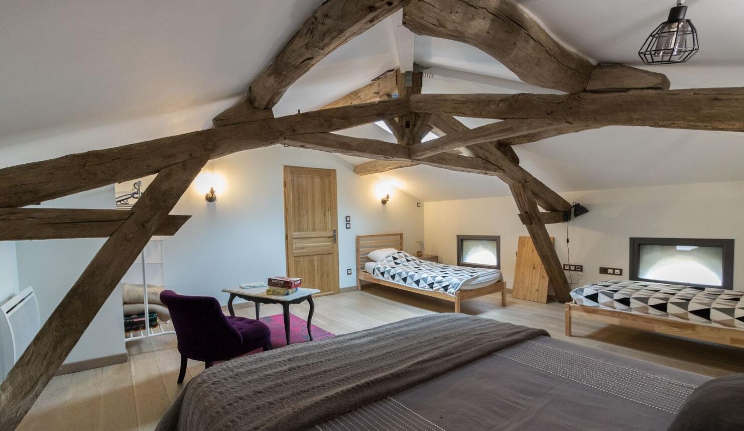 A bedroom with a sloped ceiling, wooden beams, a bed with a patterned duvet, a chair, a small table, and a television.