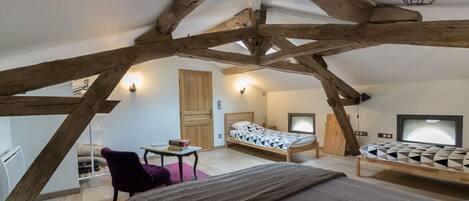 A bedroom with a sloped ceiling, wooden beams, a bed with a patterned duvet, a chair, a small table, and a television.
