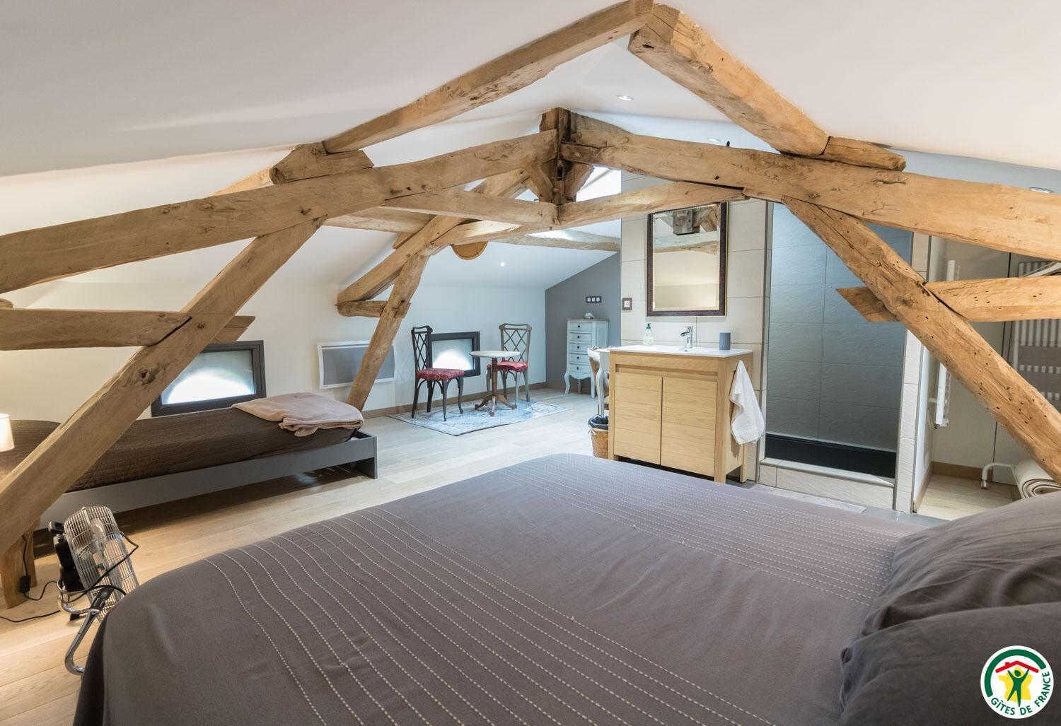 Un dormitorio con techo inclinado, una cama, un escritorio y un baño con espejo y lavabo.