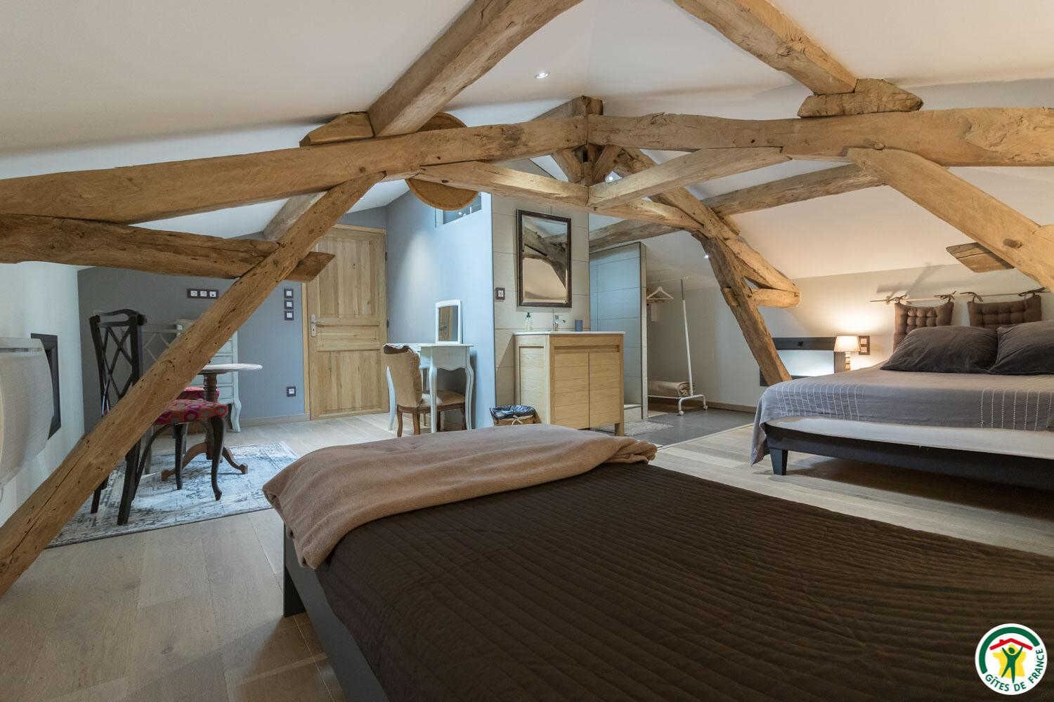 A bedroom with a large bed, a smaller bed, and a desk with a chair. There is a wardrobe and a mirror on the wall.