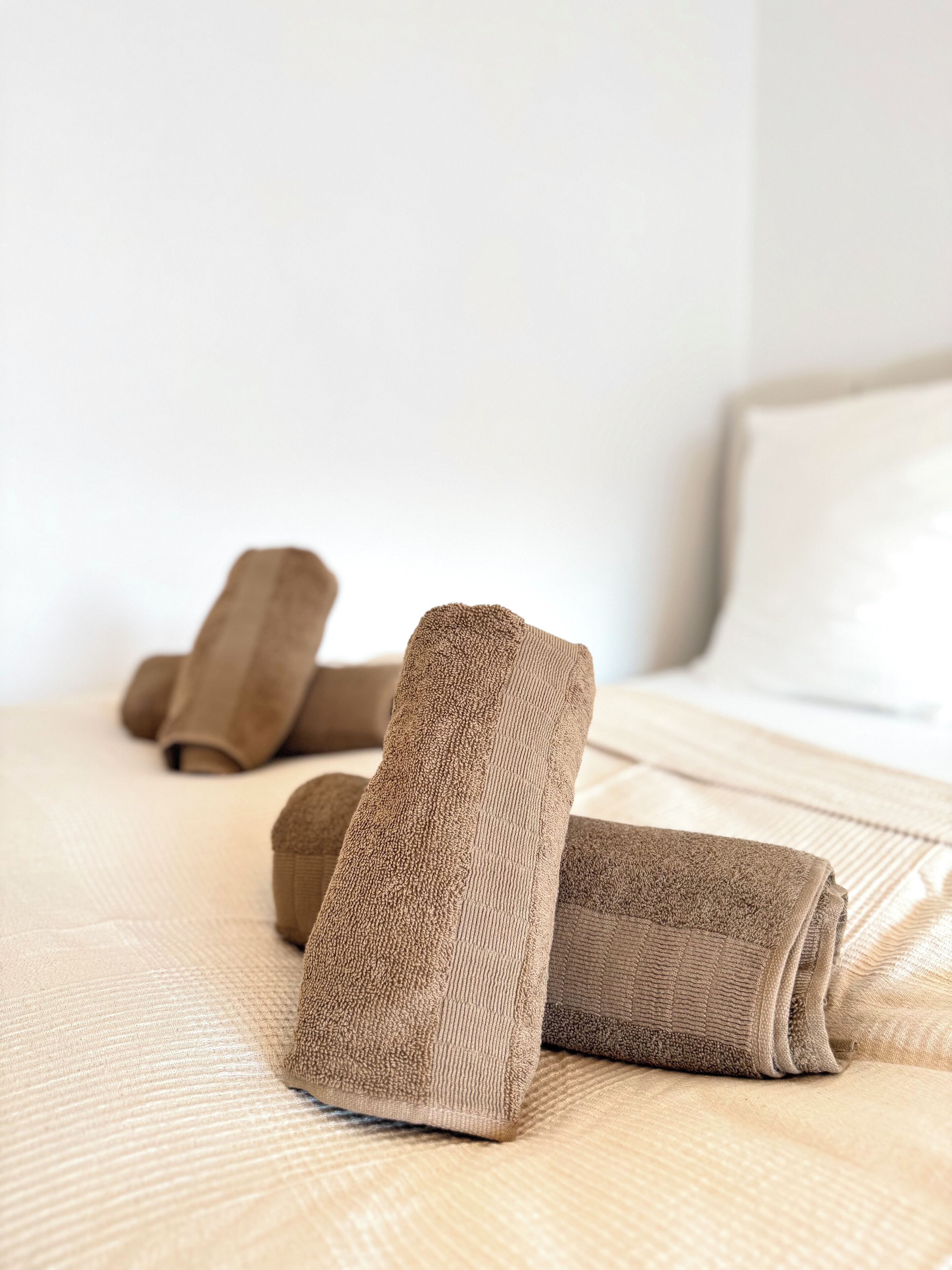 Una cama bien hecha con una colcha color beige y dos toallas enrolladas.