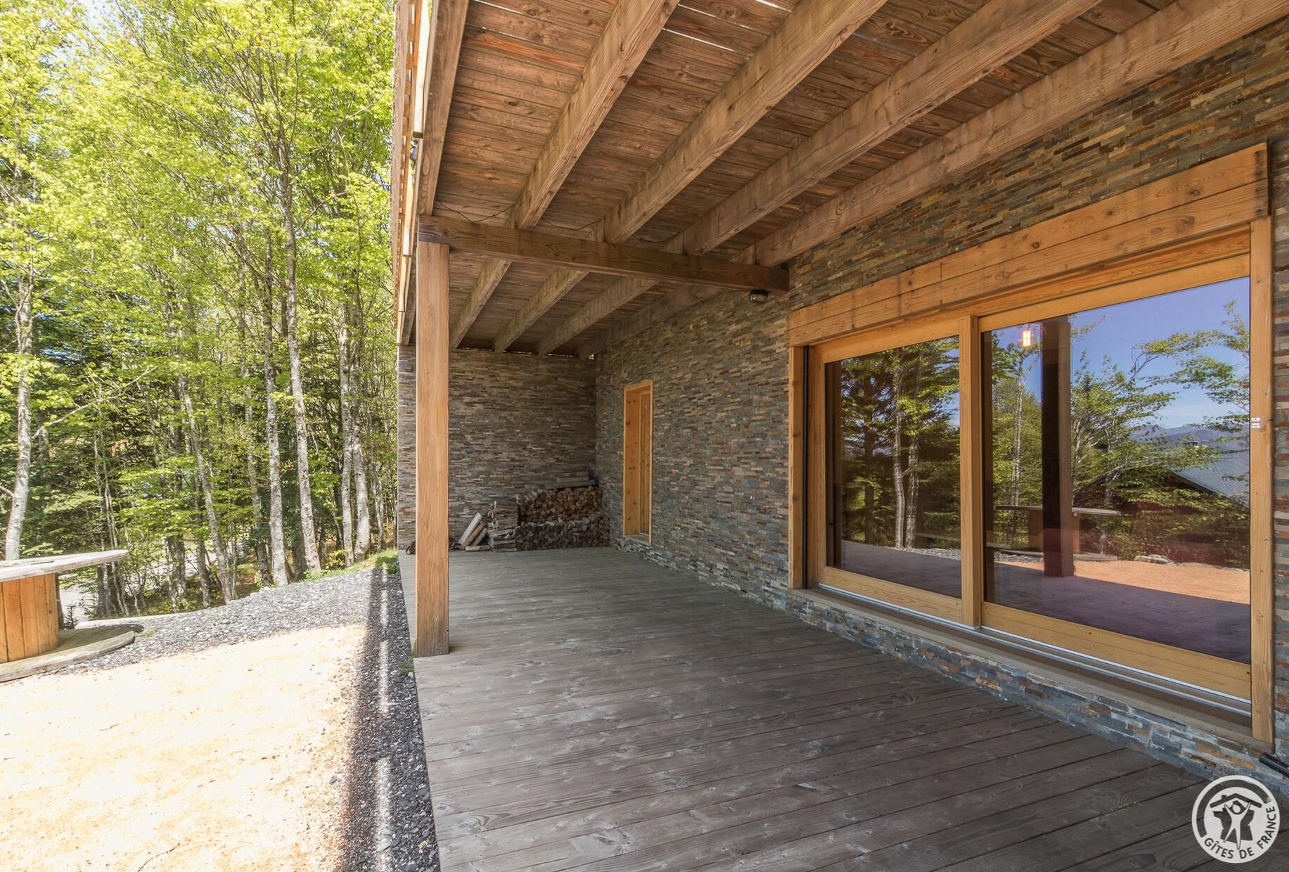 Une terrasse en bois couverte, avec des murs en pierre et de grandes fenêtres.
